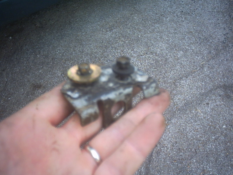 Hand holding a corroded stamped steel bracket with two bolts and a brass washer