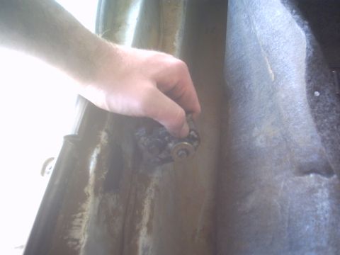 1991 Ford LTD Crown Victoria - Close-up of a bare hand gripping a rusty bolt-on hinge bracket on a stripped door jamb, with flaking surface rust and old sealer streaking…