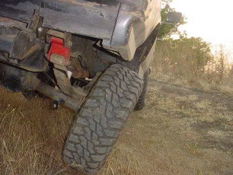 1988 Ford Bronco - Off-road vehicle's rear suspension and tire on a grassy, uneven surface.