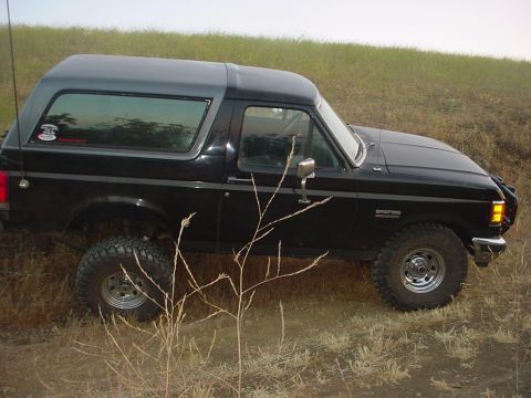 1988 Ford Bronco - This black 1988 Ford Bronco is shown from a 3/4 front angle, parked on a grassy incline.