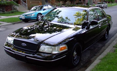 1998 Ford Crown Victoria - A black 1998 Ford Crown Victoria is parked on a residential street next to a sidewalk and grass.