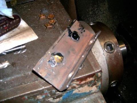1978 Ford Bronco - A small rusty steel bracket clamped in a shop bench vise, with a hole cut in it and fresh weld spatter and grinding marks across the face.…