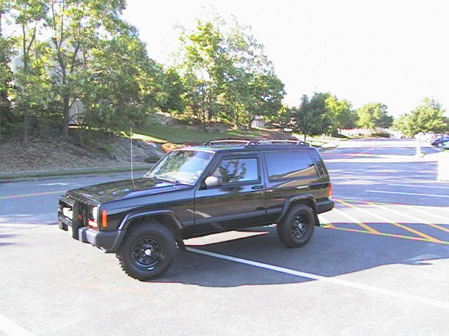 Black two-door Jeep Cherokee SUV parked in an empty lot, 3q-front view.