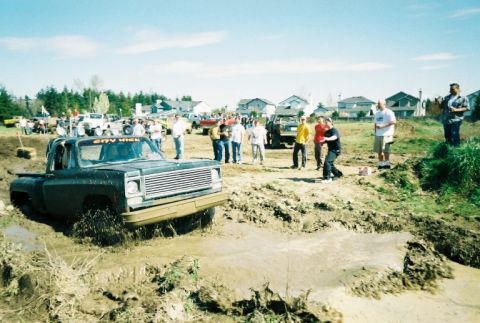 1995 Ford Bronco - A pickup truck is stuck in a mud pit during an event, with spectators gathered around.