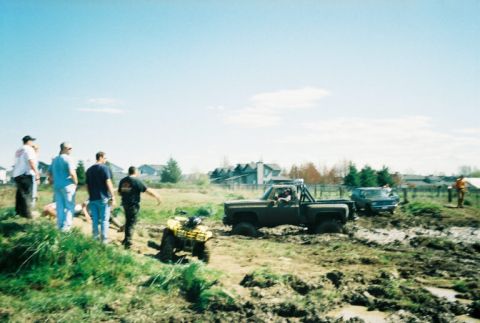 1995 Ford Bronco - A group of people observe as a dark green pickup truck and an ATV navigate a muddy terrain.