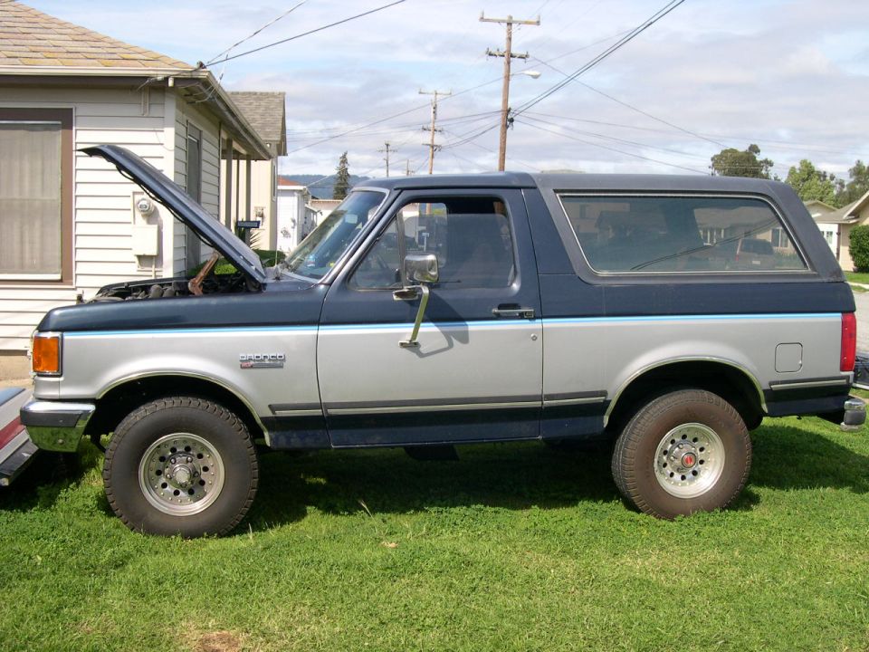 Side view of a two-tone blue and silver Ford Bronco on grass with the hood open