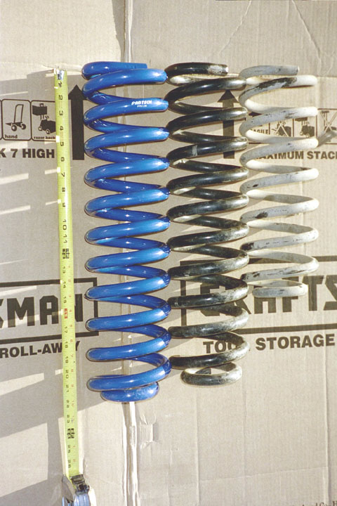 1994 Ford Bronco - Comparison of suspension spring lengths using a tape measure against a cardboard background.