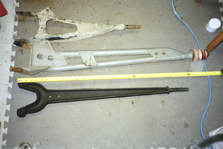 Three different automotive suspension parts laid out on a floor with a tape measure