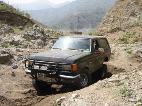 1985 Ford Bronco - This Ford Bronco is shown tackling a challenging off-road trail with steep, rocky inclines.
