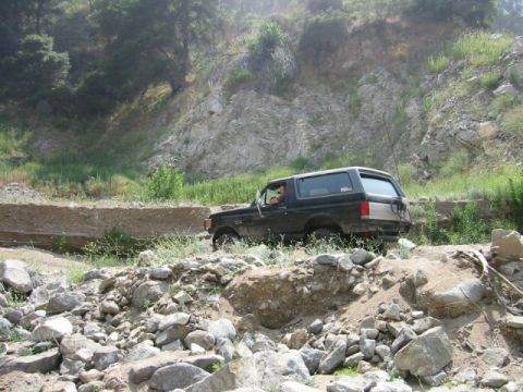 1985 Ford Bronco - A black Ford Bronco navigates a challenging off-road path with steep, rocky terrain.