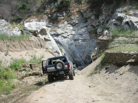 1988 Ford Bronco - This SUV navigates a narrow dirt path through a rocky canyon, its rear spare tire visible.