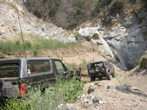 1988 Ford Bronco - Two SUVs navigate a challenging off-road path through a rocky canyon.