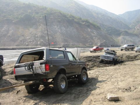 1988 Ford Bronco - Several off-road vehicles, including a 1988 Ford Bronco, are stuck in the mud near a dry riverbed.