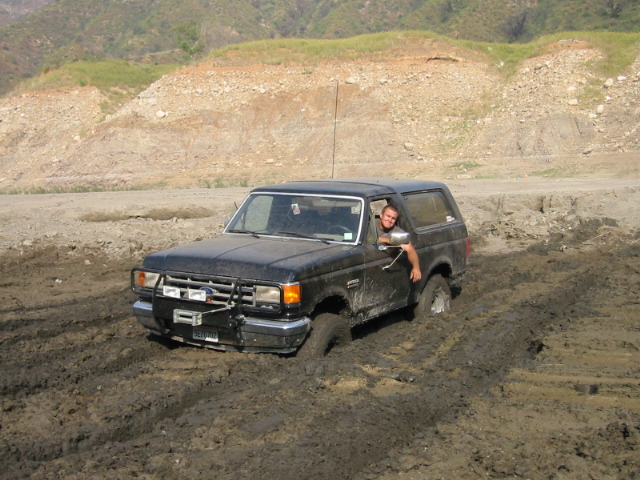 Black Ford Bronco stuck in mud, front bumper with winch, driver visible