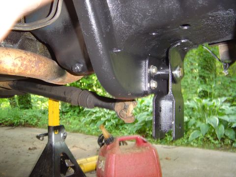 1986 Ford Bronco - Underbody view of a vehicle showing a freshly painted black frame bracket with mounting bolts, alongside a rusty exhaust pipe and driveshaf…