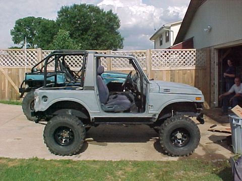 1978 Ford Bronco - A modified Suzuki Samurai is parked outside a garage with another vehicle visible behind it.