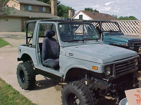 1978 Ford Bronco - Two off-road vehicles are parked in a driveway, one gray and one blue, with houses in the background.
