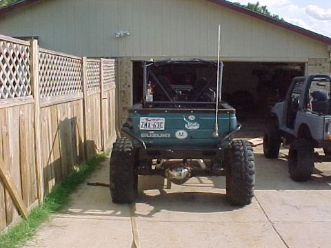 1978 Ford Bronco - Two off-road vehicles are parked in front of a garage, one is a modified Suzuki Samurai.