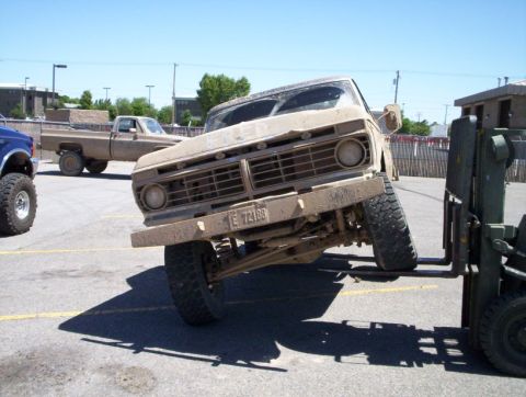1978 Ford Bronco - A tan Ford F-Series truck is being lifted by a forklift in a parking lot with other vehicles present.