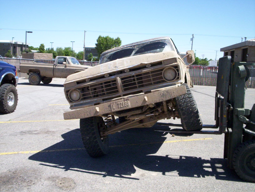 Tan Ford F-Series truck lifted by forklift, front view, grille visible