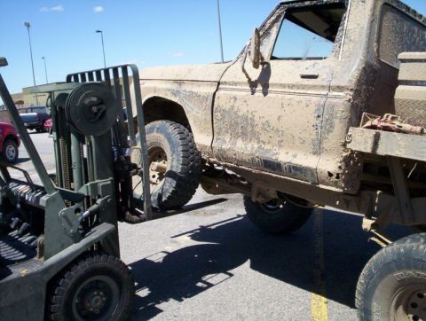 1978 Ford Bronco - A mud-caked 1978 Ford Bronco is hoisted by a forklift, revealing its weathered condition.