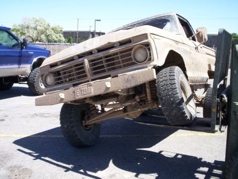 1978 Ford Bronco - A tan pickup truck is lifted for service, with another blue truck visible in the background.