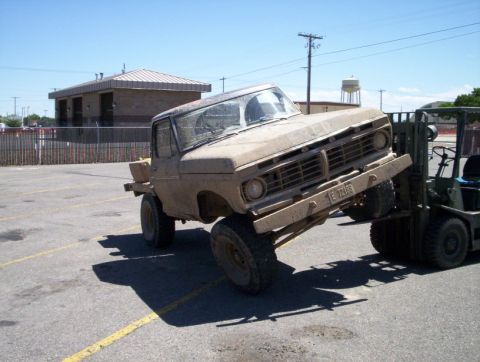 1978 Ford Bronco - A forklift lifts a dusty Ford F-Series truck, showing its front grille and license plate.