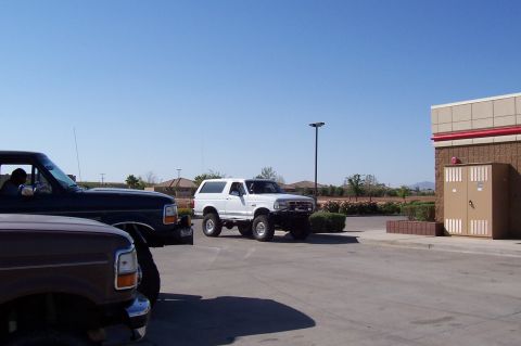 1992 Ford Bronco - A white 1992 Ford Bronco is parked in a lot with other vehicles under a clear blue sky.