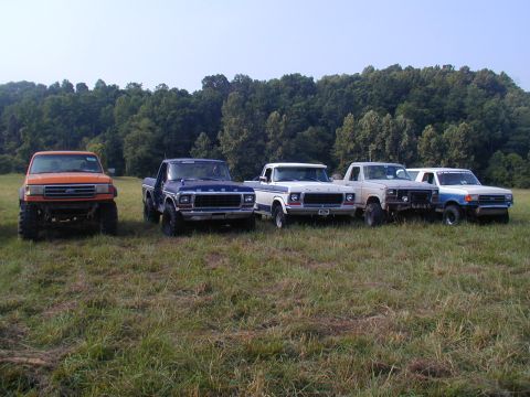 1988 Ford Bronco - A lineup of vintage Ford pickup trucks sits in a field under a clear sky.