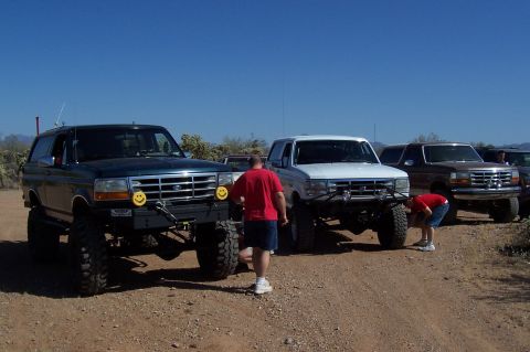 1992 Ford Bronco - A lifted 1992 Ford Bronco is parked alongside other trucks in a desert landscape.