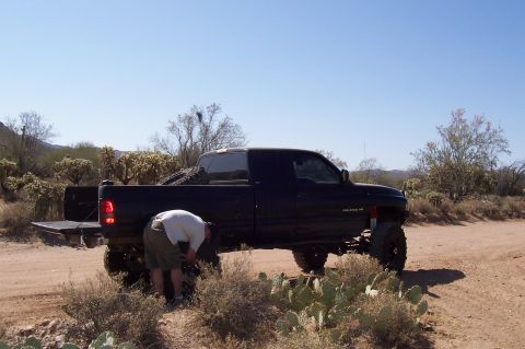 1992 Ford Bronco - Lifted Dodge Ram pickup truck in a desert setting with a person working on the rear tire.