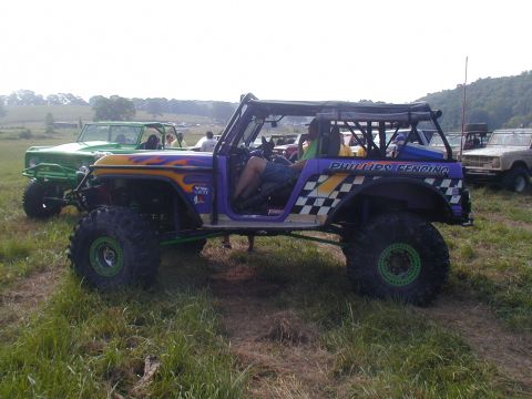 1988 Ford Bronco - Modified off-road vehicles are parked in a grassy field on a sunny day.