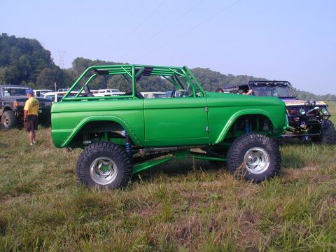 1988 Ford Bronco - A modified green SUV with a roll cage sits in a grassy field next to other off-road vehicles.