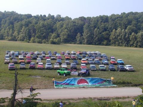 1988 Ford Bronco - A large gathering of SUVs are parked in a grassy field, with a banner spread out before them.