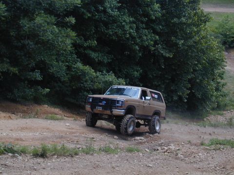 1988 Ford Bronco - This lifted Ford Bronco navigates an off-road trail with trees in the background.