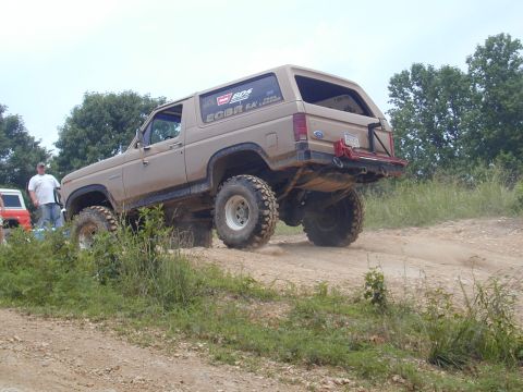 1988 Ford Bronco - A lifted Ford Bronco navigates a dusty off-road trail, kicking up dirt as it goes.