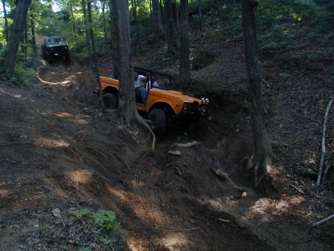 1988 Ford Bronco - Two off-road vehicles tackle a challenging dirt path in a wooded area.
