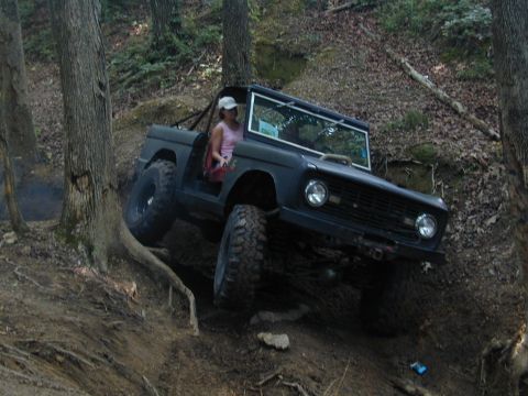 1988 Ford Bronco - This SUV is navigating a challenging off-road trail, demonstrating its climbing capabilities on a steep, muddy incline.