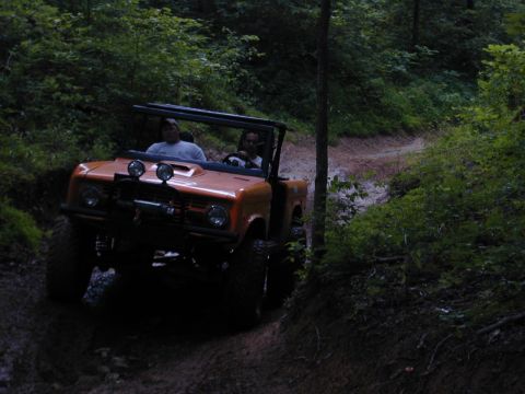 1988 Ford Bronco - Off-road vehicle navigates a wooded dirt path with two occupants.