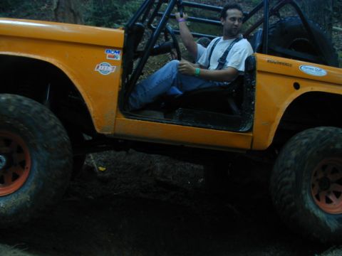 1988 Ford Bronco - An orange off-road vehicle with a roll cage is driven by a man on a dirt path.
