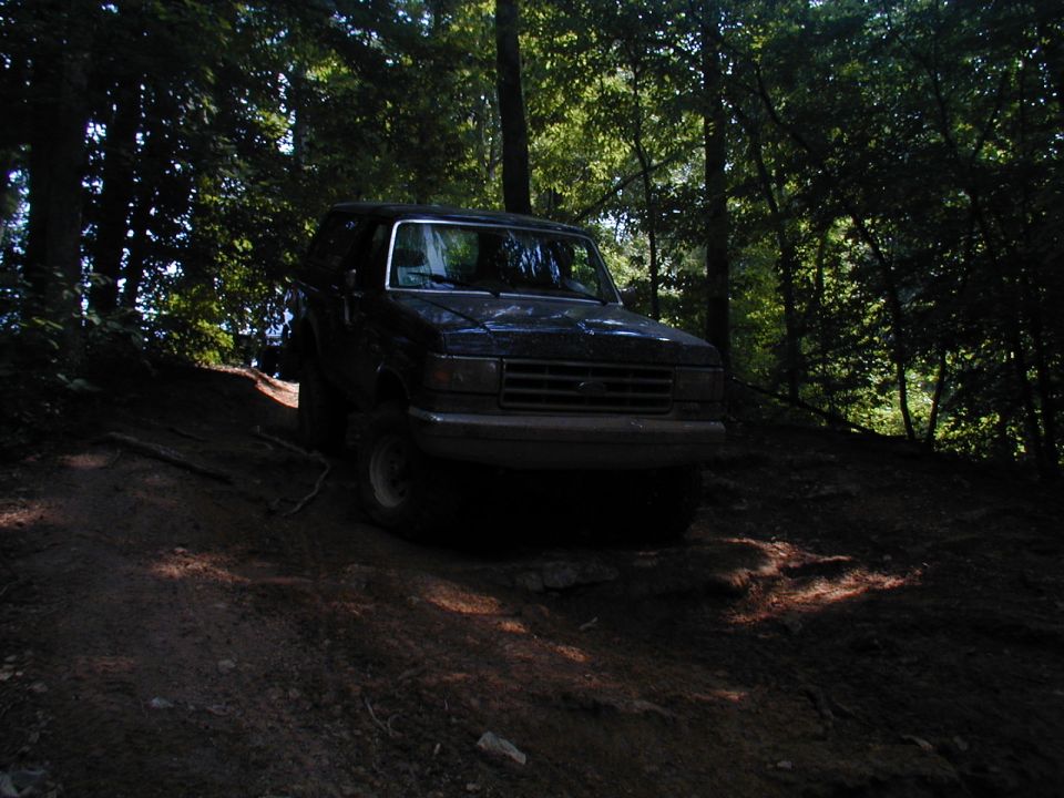 Dark Ford Bronco driving on a dirt path in a wooded area