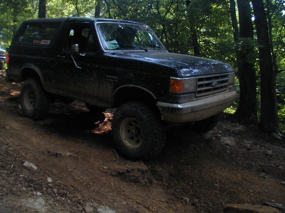 Black 1988 Ford Bronco climbing a dirt trail in a wooded area