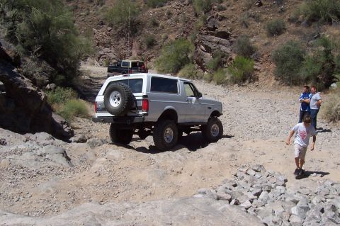 1992 Ford Bronco - A silver 1992 Ford Bronco navigates a challenging off-road path with other vehicles and people present.