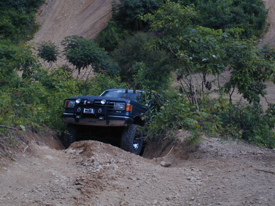 Dark colored SUV navigating a steep dirt path with trees and brush on either side. It has a brush guard and off-road tires