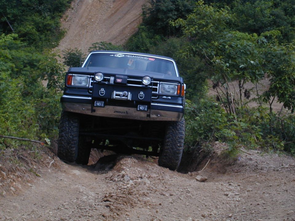 Dark blue Ford Bronco with a winch and off-road tires climbing a dirt hill