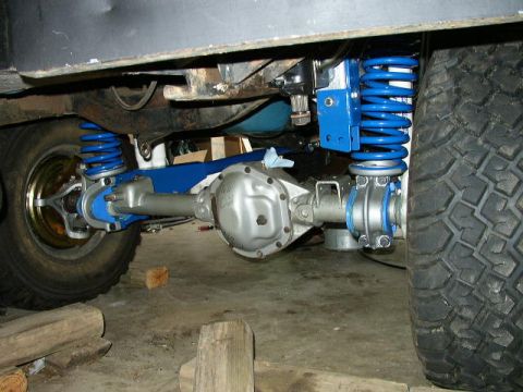1995 Ford Bronco - Close-up view of the rear axle and suspension system, bright blue springs and silver-finished components.