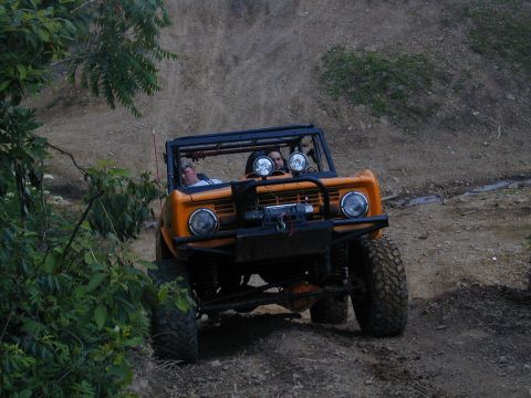 1988 Ford Bronco - This orange first-generation Ford Bronco navigates a dirt trail with its occupants.
