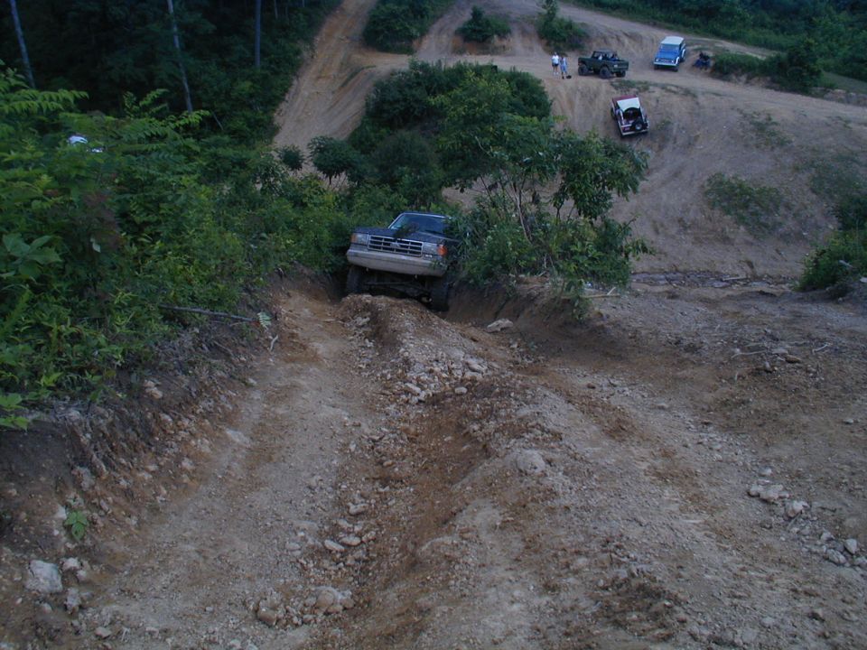 1988 Ford Bronco navigating a steep dirt trail with other vehicles visible in the background