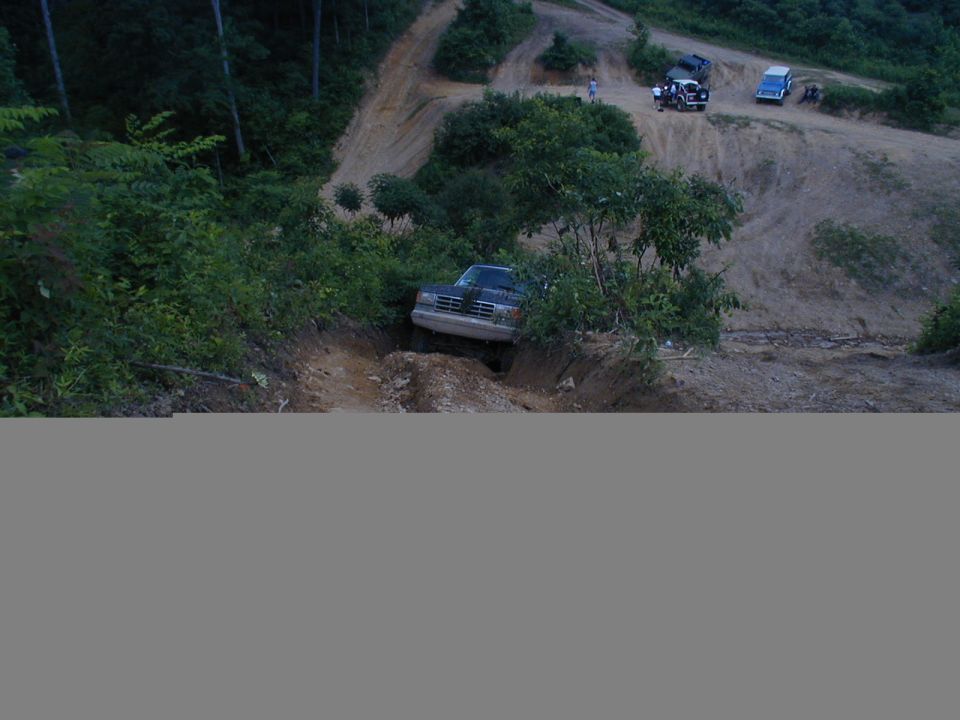 Truck going down a steep dirt trail, with other vehicles on a ridge above