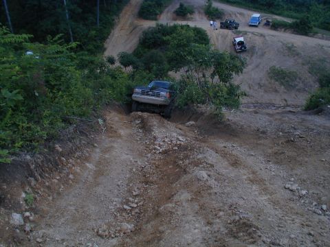 1988 Ford Bronco - A dark blue Ford Bronco tackles a challenging dirt path, with other vehicles visible further up the trail.